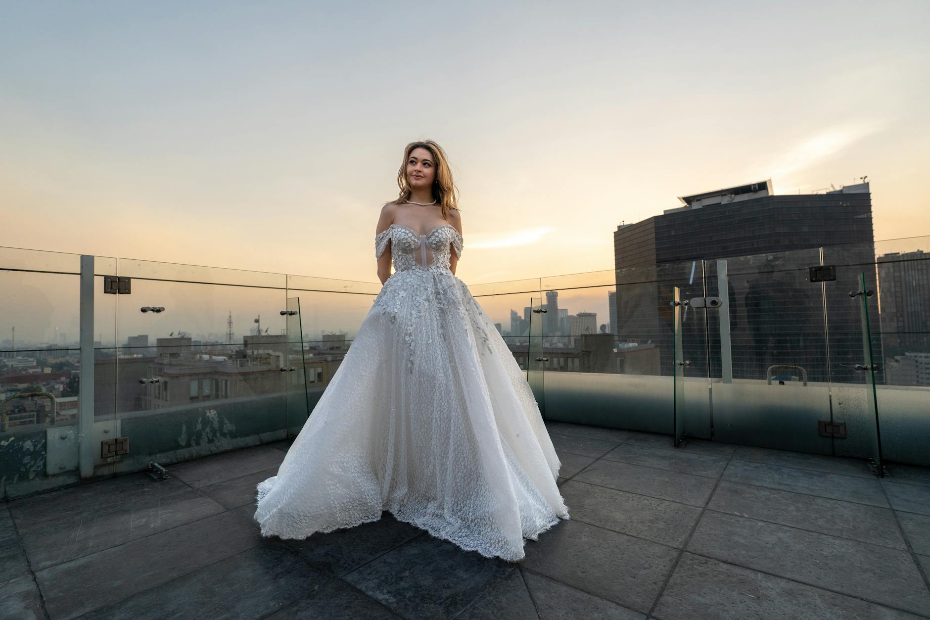 Panna młoda na dachu wieżowca z panoramą miasta o zachodzie słońca