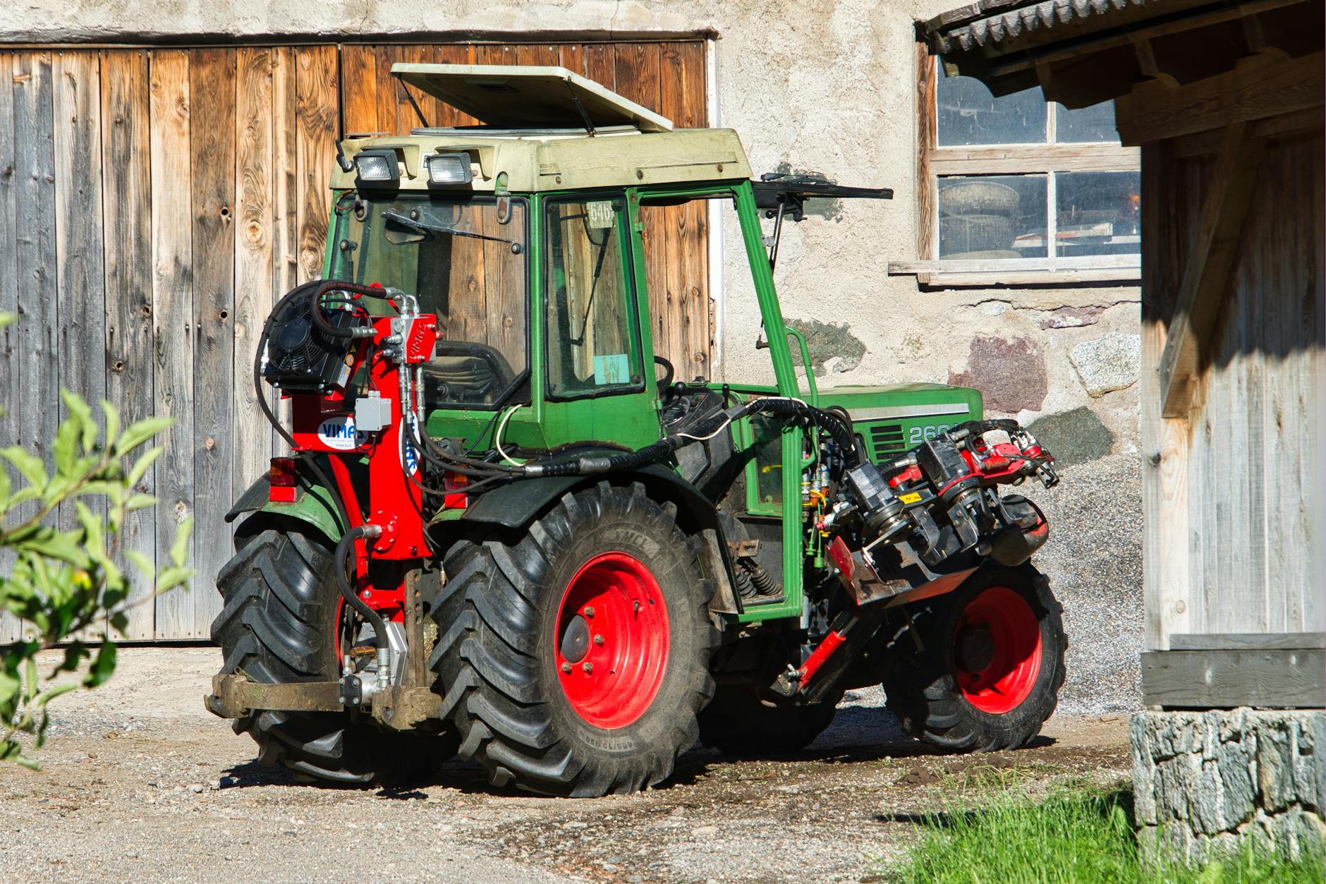 Zielony ciągnik rolniczy z oponami na słonecznym podwórzu gospodarstwa