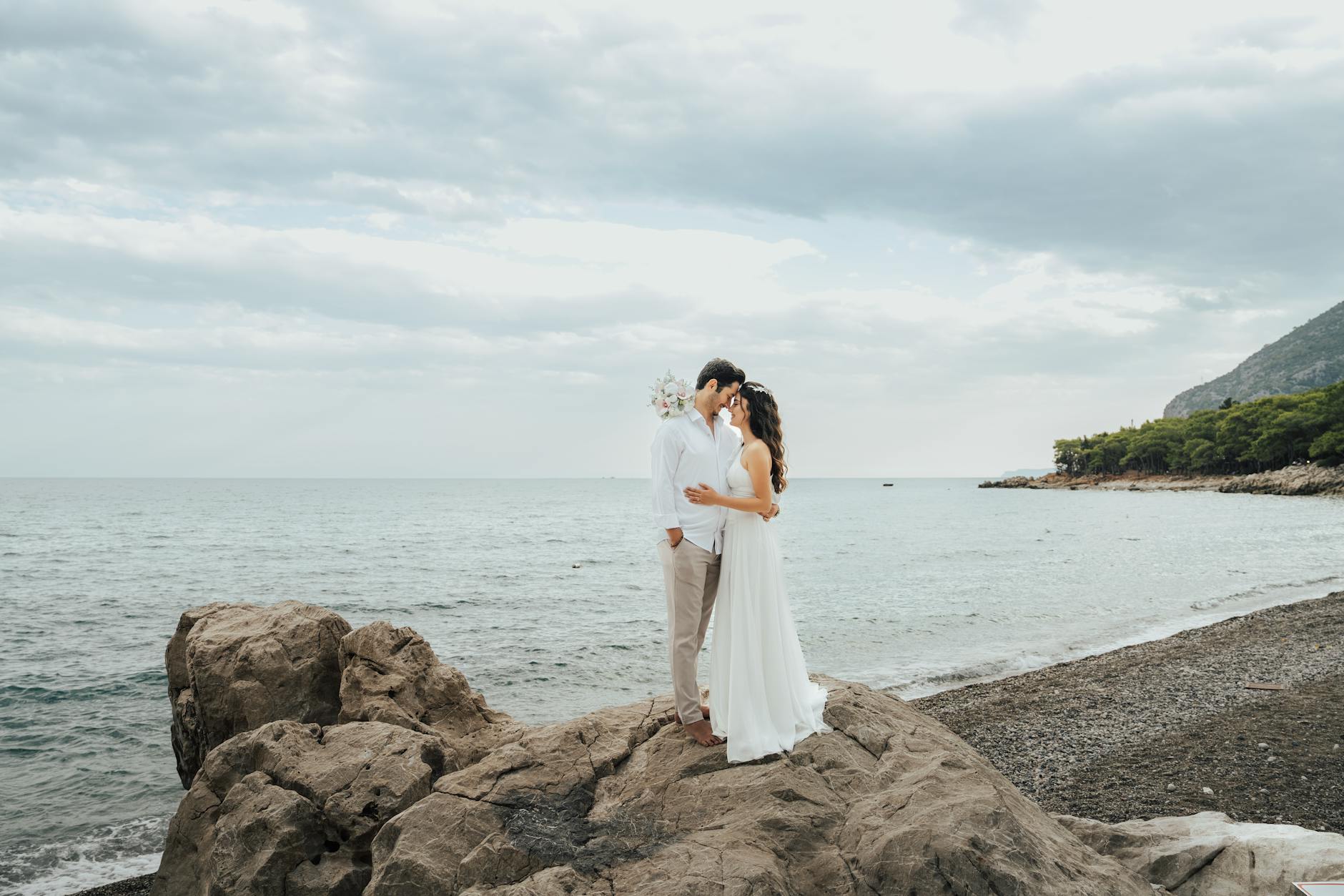 Para młoda obejmuje się na skalistym wybrzeżu podczas ślubnej ceremonii