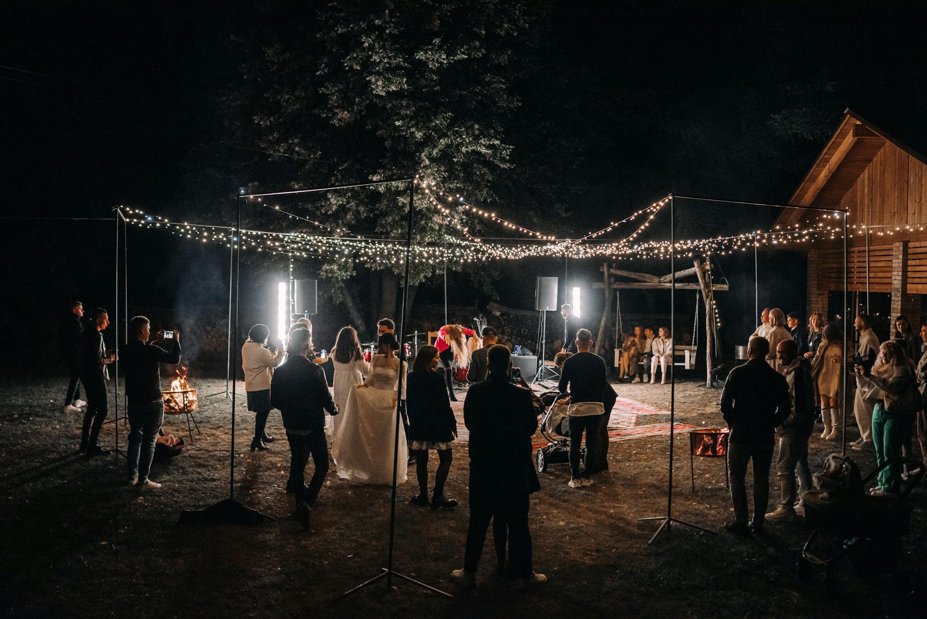 Goście bawiący się na nocnym przyjęciu weselnym w ogrodzie pod girlandami